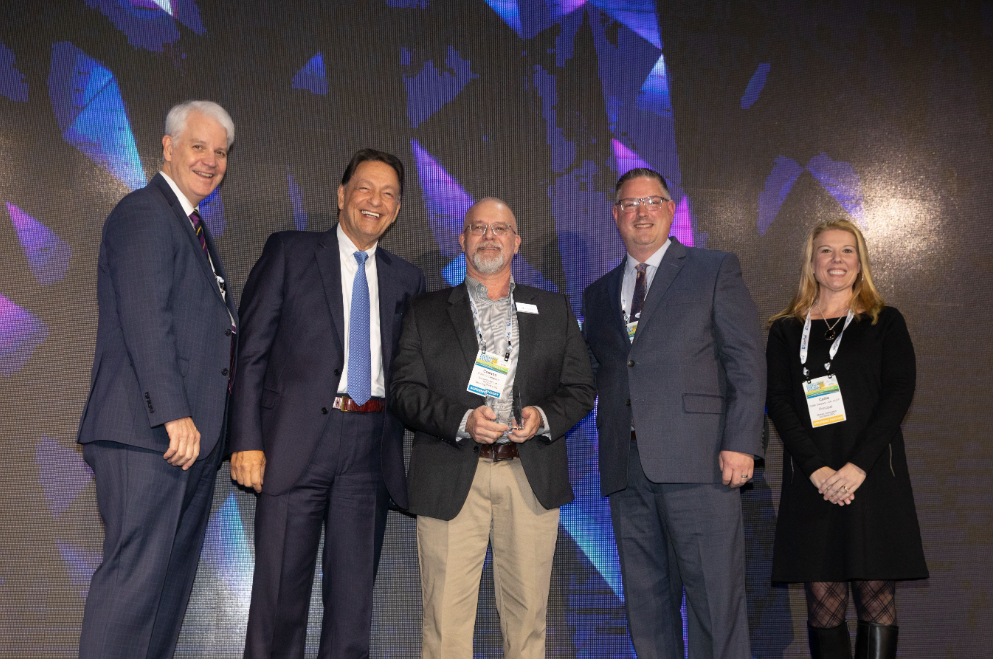 Dr. Tangorra holding an award on stage with two men standing to his right and one man and one woman standing to his left