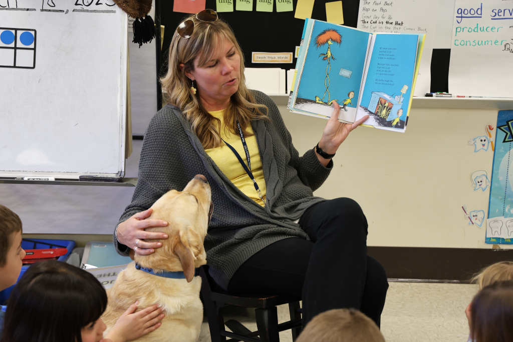 teacher reading to a group of first grade students and a yellow lab dog